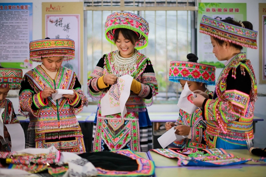 2025年12月16日,贵州省黔西市太来彝族苗族乡院子小学的学生在民间刺绣艺人(右三)的指导下学习刺绣技艺。.jpg